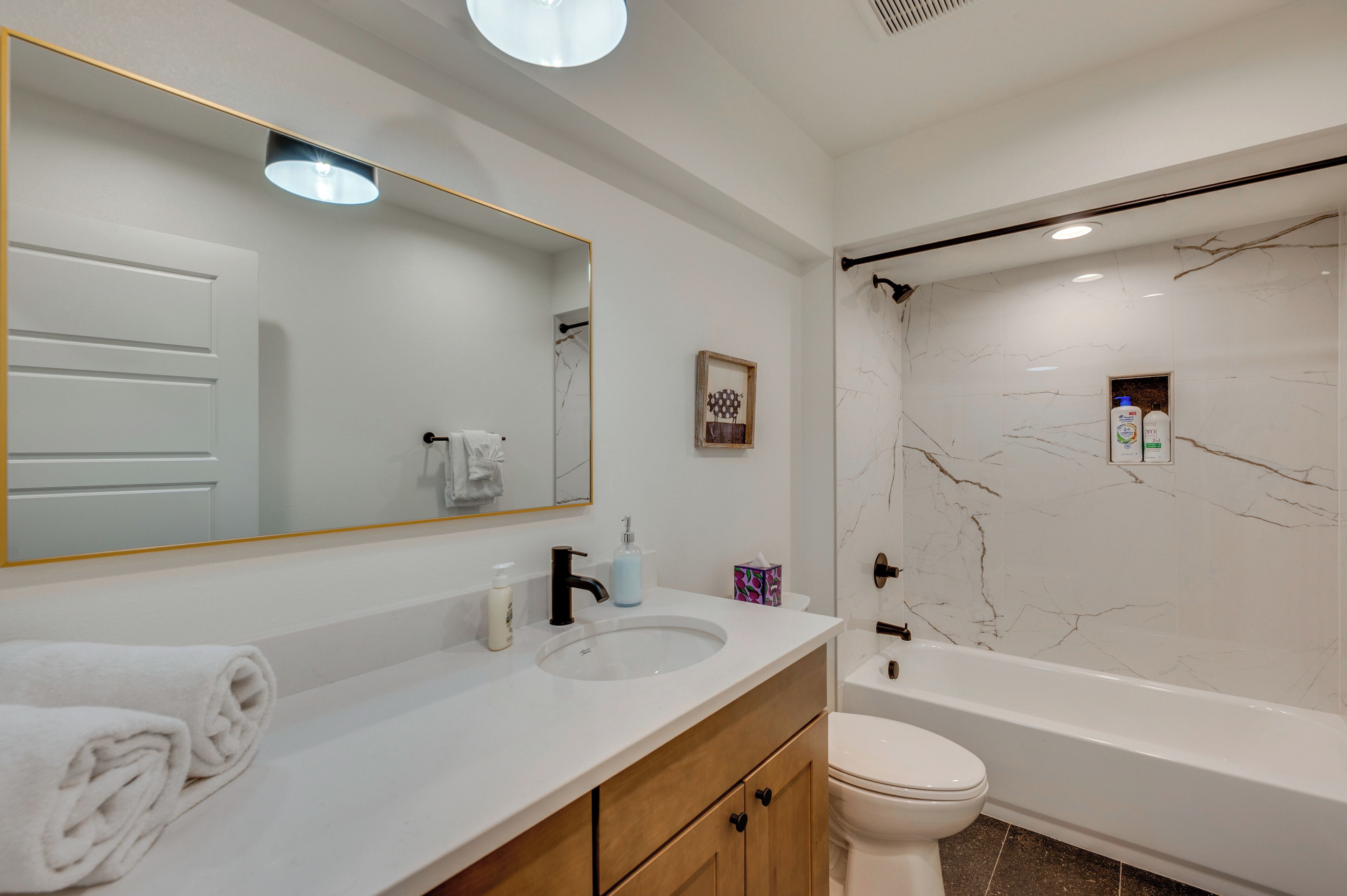 A modern bathroom with a white marble wall, a large mirror, a white sink, a toilet, and a bathtub.
