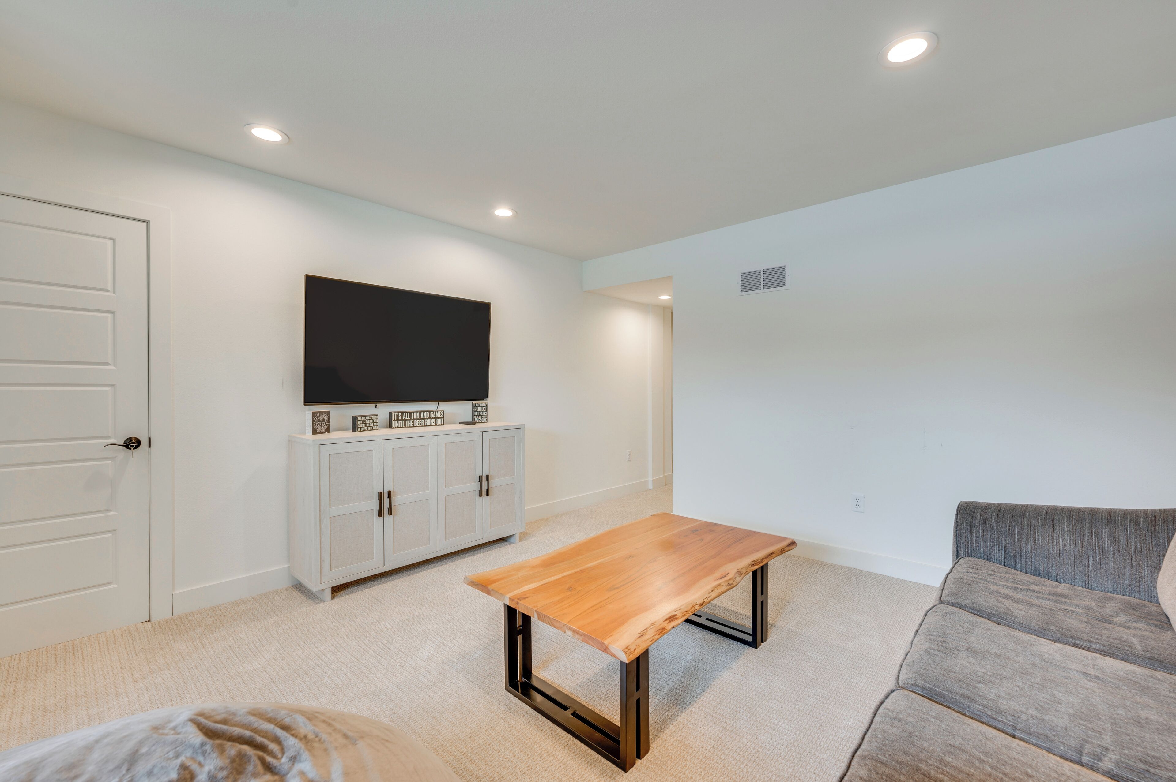 A modern living room with a wooden coffee table, grey sofa, white cabinet, and a flat-screen TV mounted on the wall.