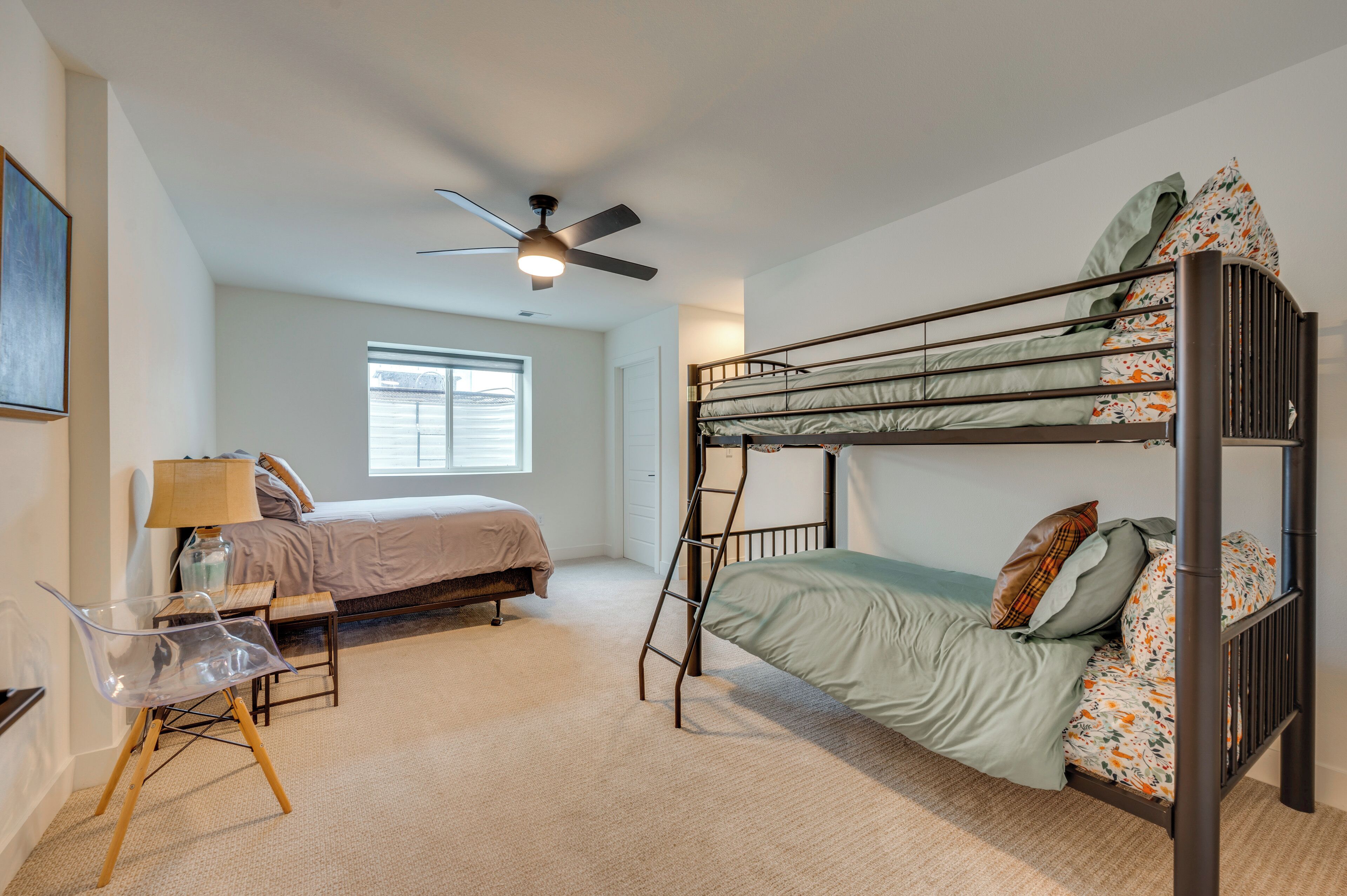 A bedroom with bunk beds, a desk, a chair, a ceiling fan, and a window.