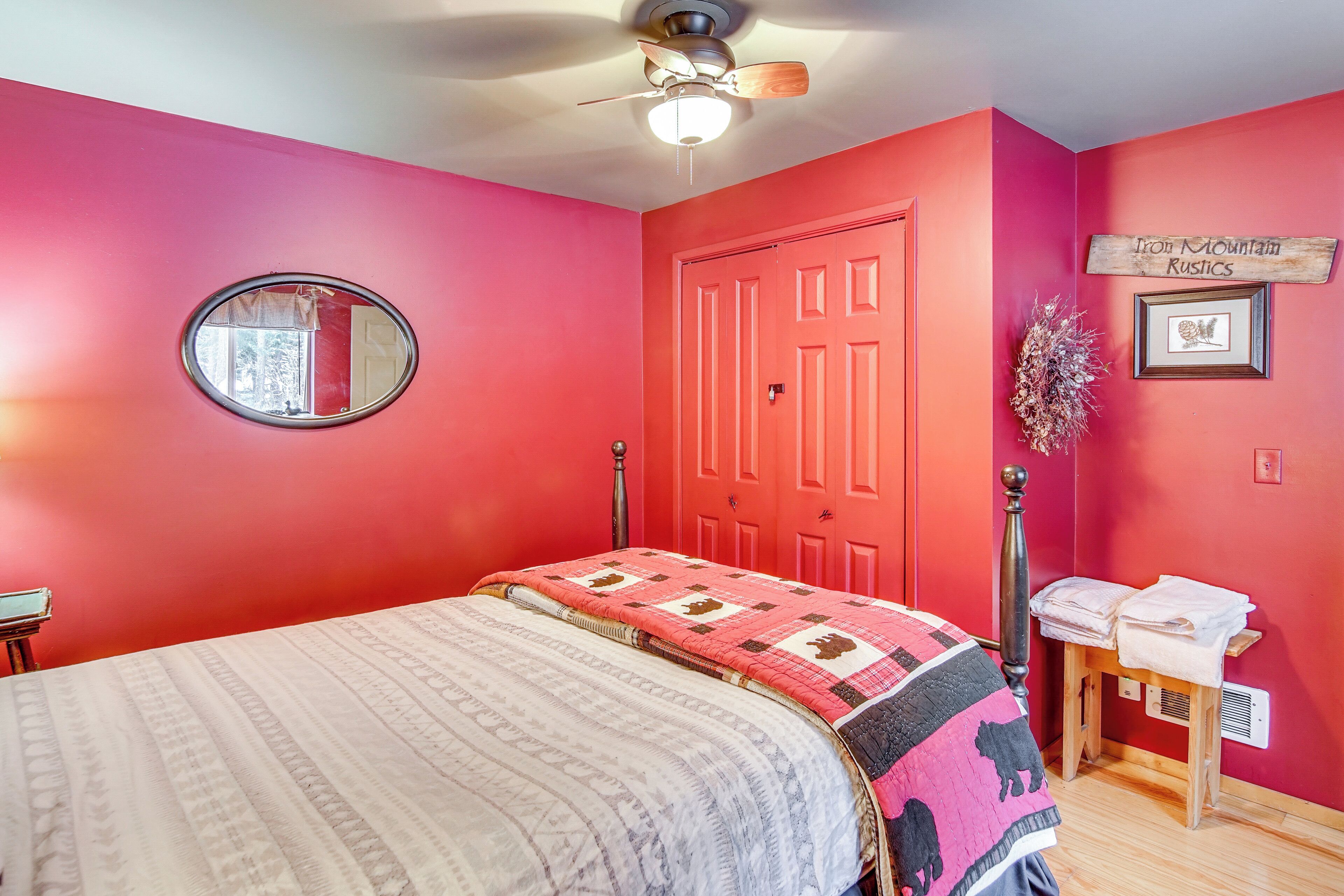 A bedroom with a bed, a round mirror, a red door, and a small table with towels.