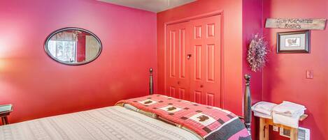 A bedroom with a bed, a round mirror, a red door, and a small table with towels.