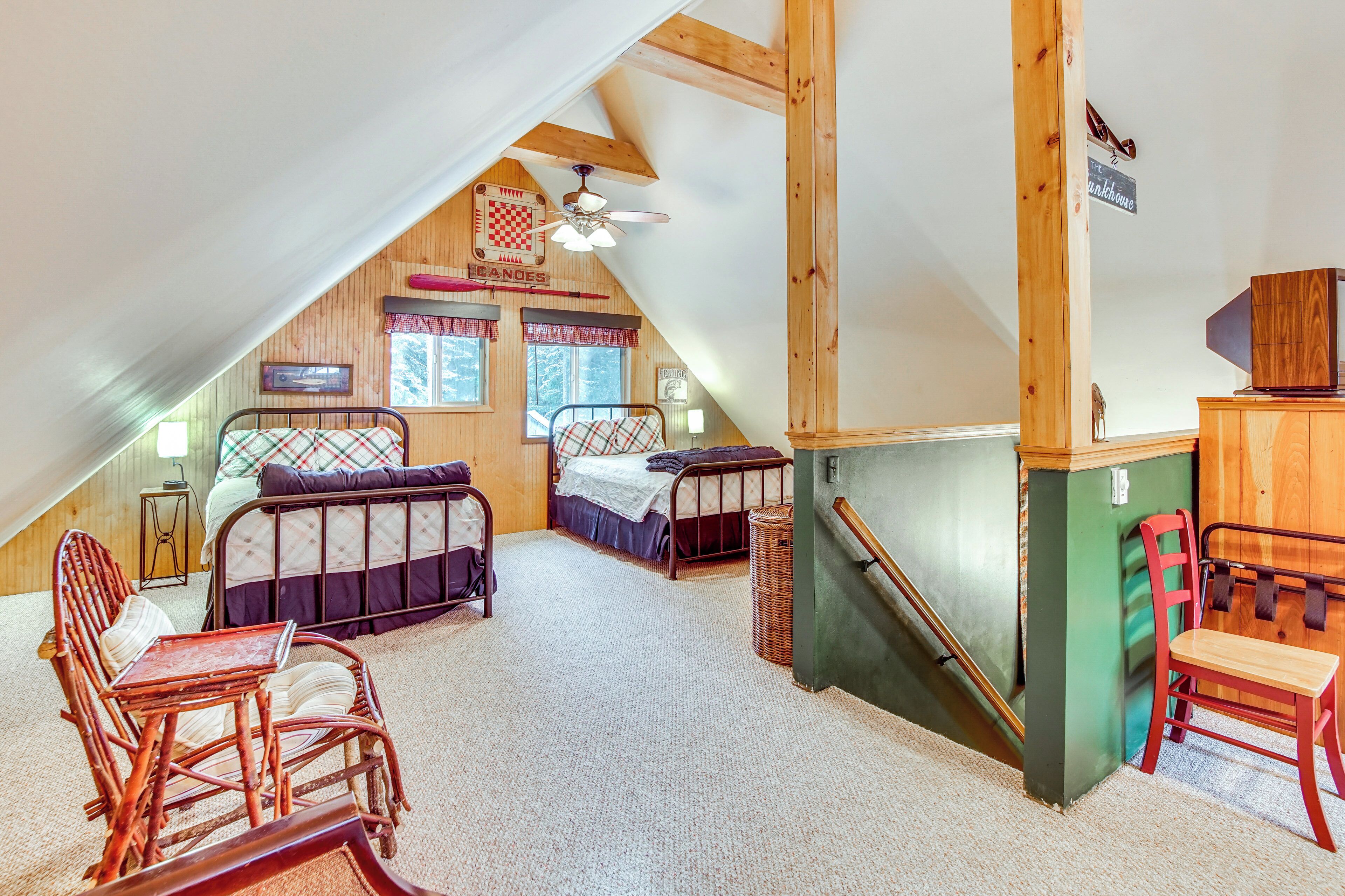 A cozy attic bedroom with two beds, a wooden ceiling, and a small table.