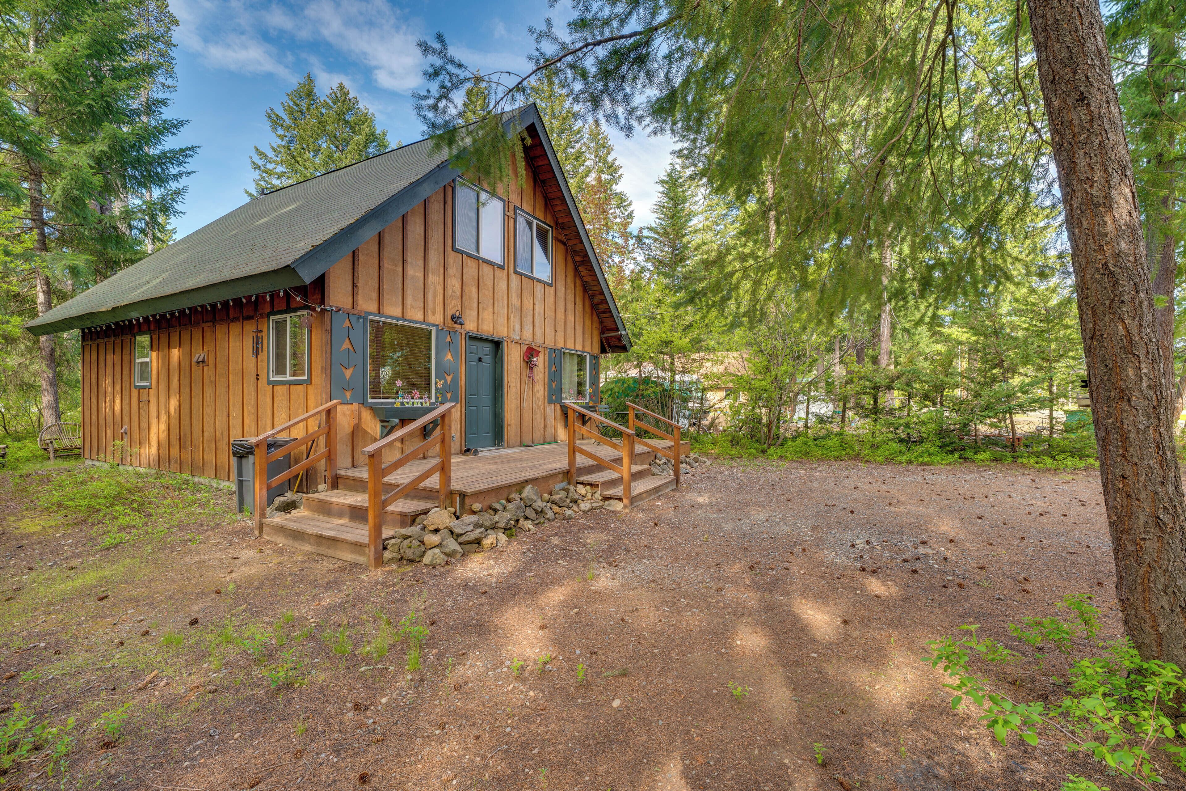 Eine Holzhütte mit Veranda und Feldweg, umgeben von Bäumen.
