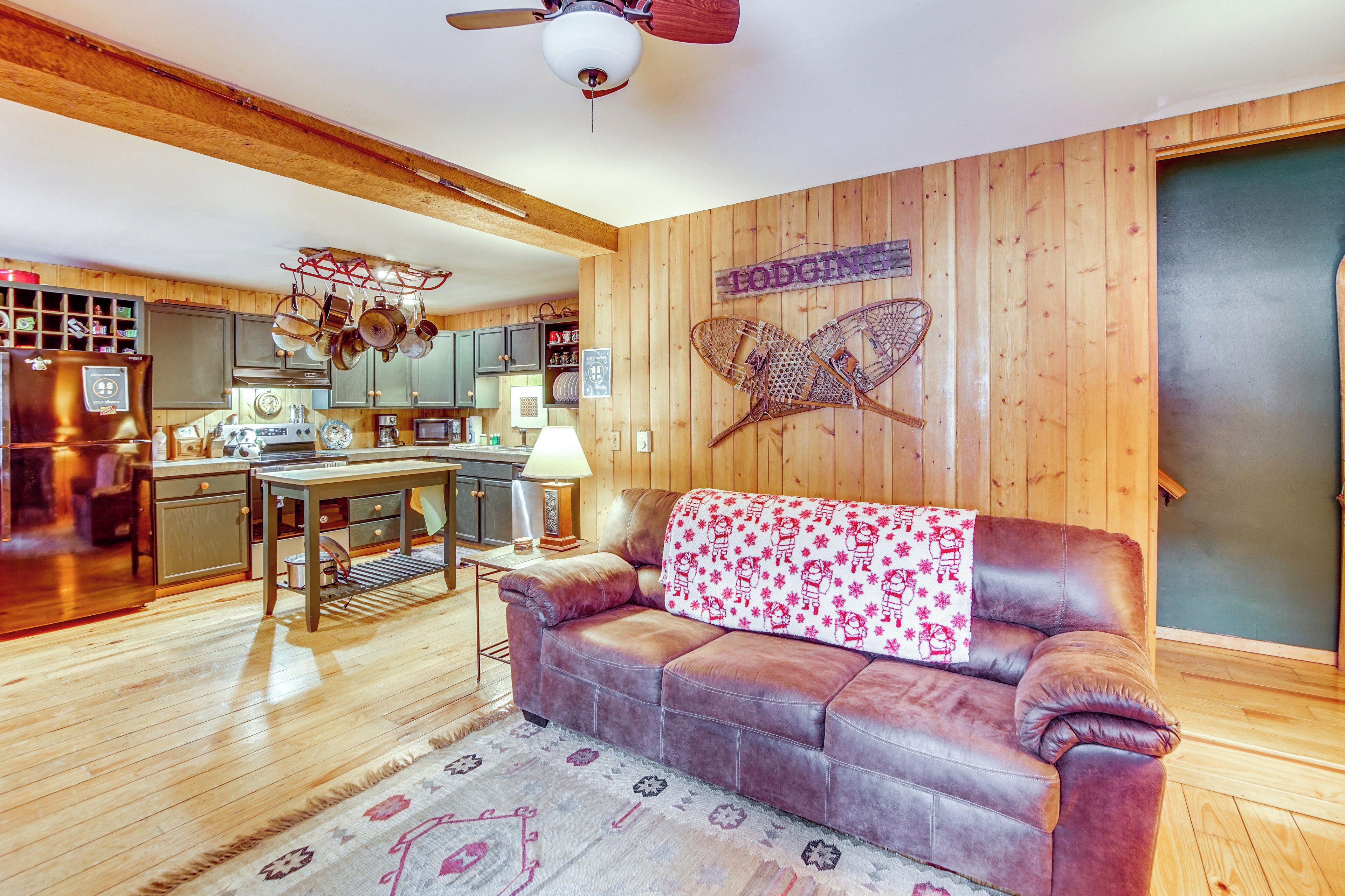 A cozy living room with a leather sofa, wooden walls, and a kitchen in the background.