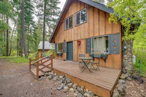 A wooden cabin with a deck, a dining area with a table and chairs, and a stone wall. - 1 Mi to Lake Easton: Cozy Cascades Cabin! (Easton)