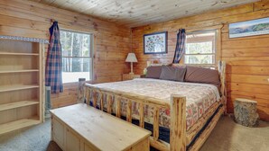 A wooden cabin bedroom with a bed, a bedside table, a lamp, and a window with curtains. - 2 Mi to Skiing: Casper Cabin w/ Mtn Views! (Casper)
