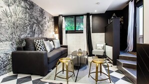 A modern living room with a black sofa, two stools, a coffee table, and a large mural.