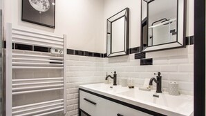 A bathroom with a white tiled wall, a white vanity with black handles, a white towel rack, and two mirrors.