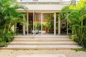 A modern house with a covered outdoor area, steps leading to a patio, and lush greenery.