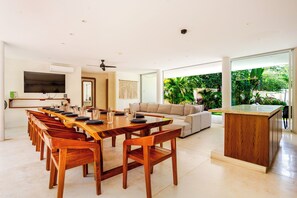 A modern dining area with a long wooden table, multiple chairs, a sofa, and a kitchen island.