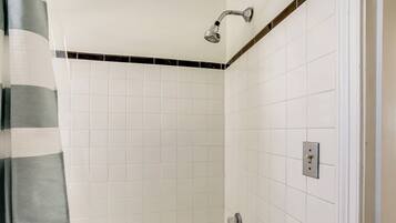 A bathroom with white tiled walls, a showerhead, a towel rack, and a light switch.