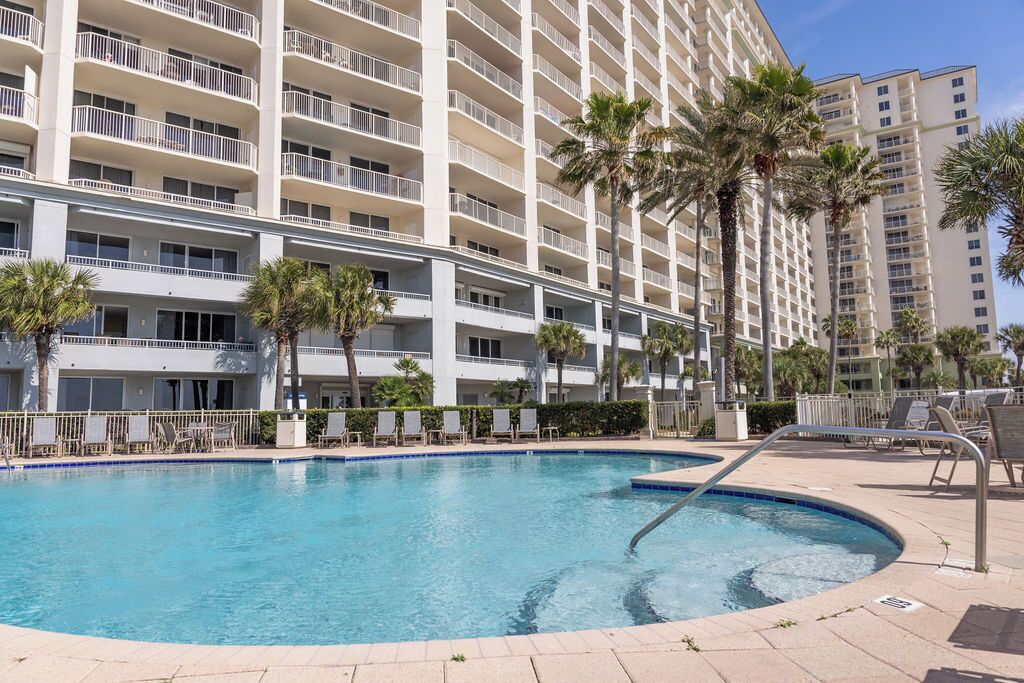 Un hôtel doté d’une grande piscine, de palmiers et d’un immeuble à plusieurs étages avec des balcons.