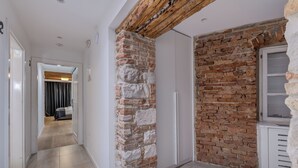 A hallway with a stone column, a brick wall, and a white door leading to a room with a bed and curtains. - The Code Luxury Rooms (Split)