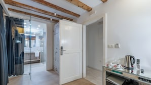 A hotel room with a wooden ceiling, a glass partition, a white door, a minibar, and a small table with a kettle and cups. - The Code Luxury Rooms (Split)