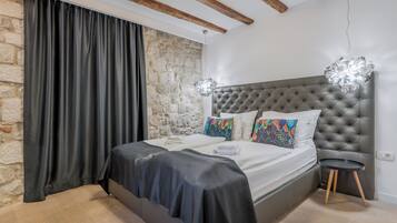 Un dormitorio con una cama grande, pared de piedra, vigas de madera y una lámpara moderna.
