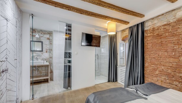 A modern bedroom with a large bed, a glass shower enclosure, and a brick wall. - The Code Luxury Rooms (Split)