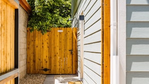 A narrow pathway leading to a wooden gate with a 'PRIVATE' sign, flanked by a brick wall and a wooden fence, with a concrete path and a doormat on the ground. - < 1 Block to City Park: New-build Apt in Denver! (Denver)