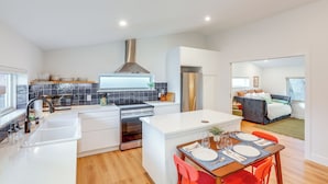 A modern kitchen with white cabinetry, a stainless steel range hood, and a dining area with a table set for two. - < 1 Block to City Park: New-build Apt in Denver! (Denver)