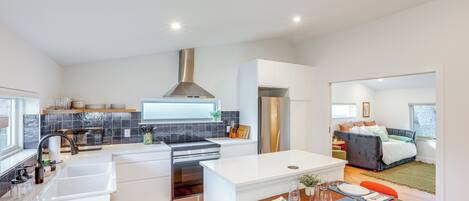 A modern kitchen with white cabinetry, a stainless steel range hood, and a dining area with a table set for two.