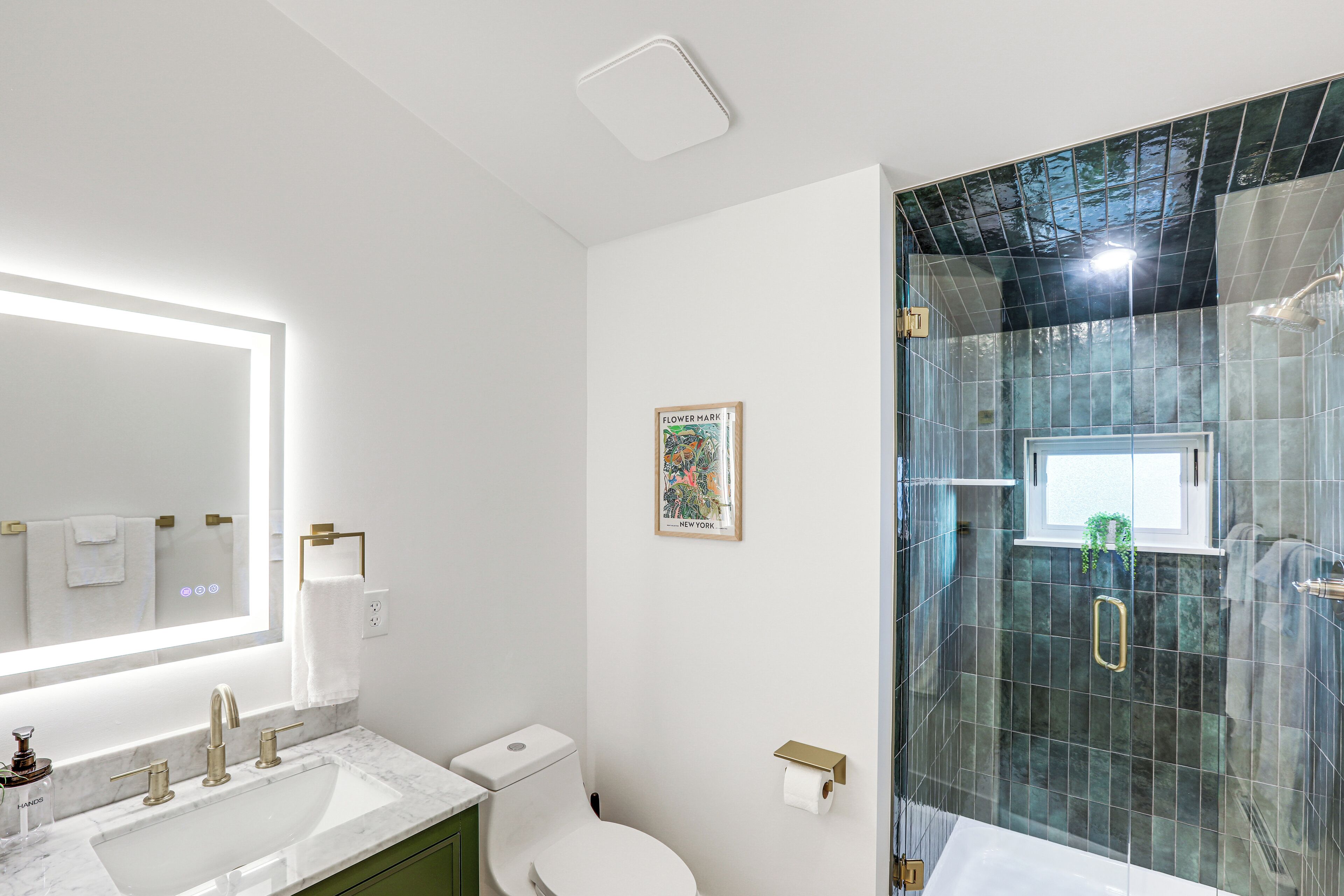 Une salle de bain moderne avec un grand miroir, deux lavabos, des toilettes et une douche séparée par une paroi de verre.