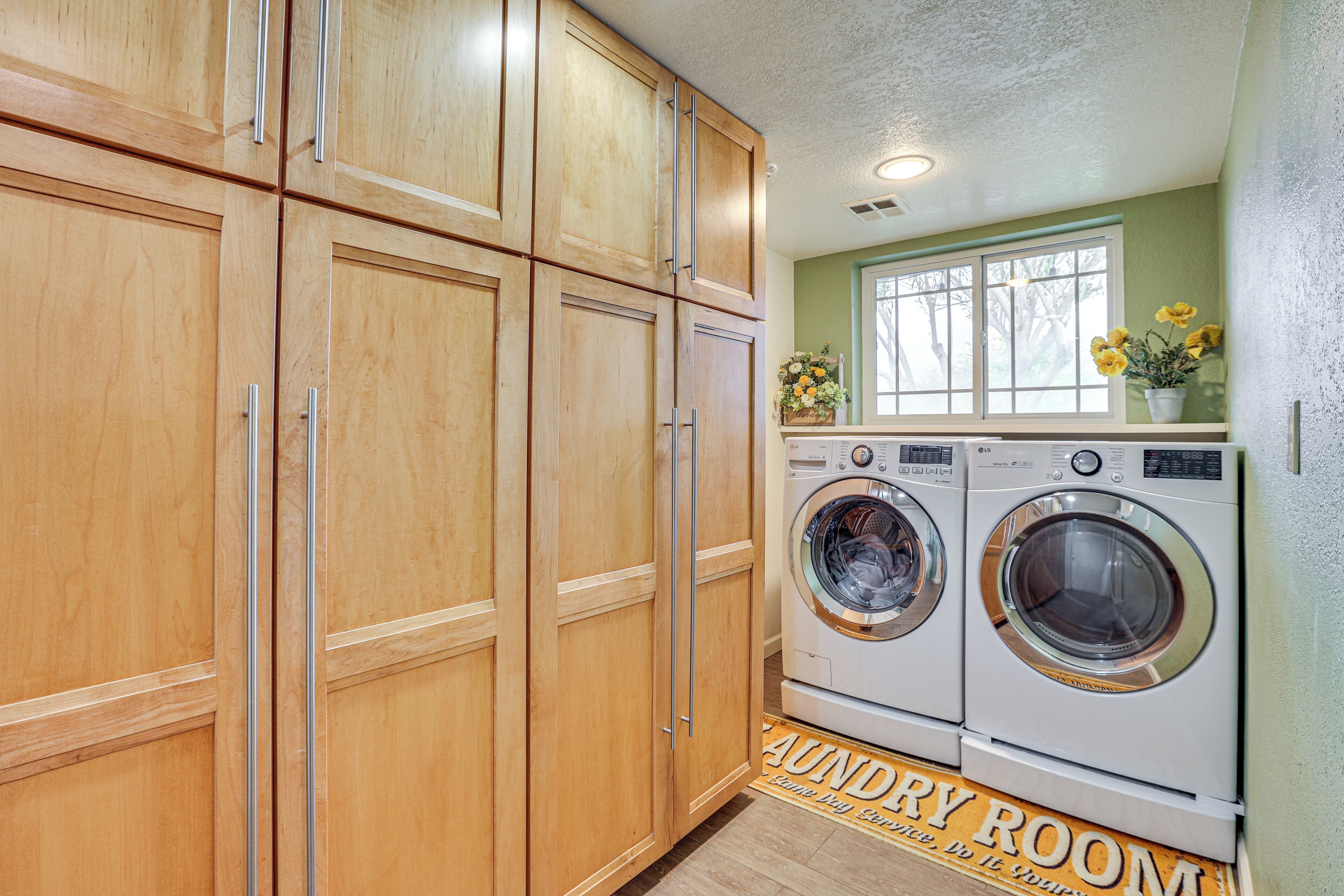 A laundry room with wooden cabinets, two front-loading washing machines, a window with a view, and a sign on the floor.