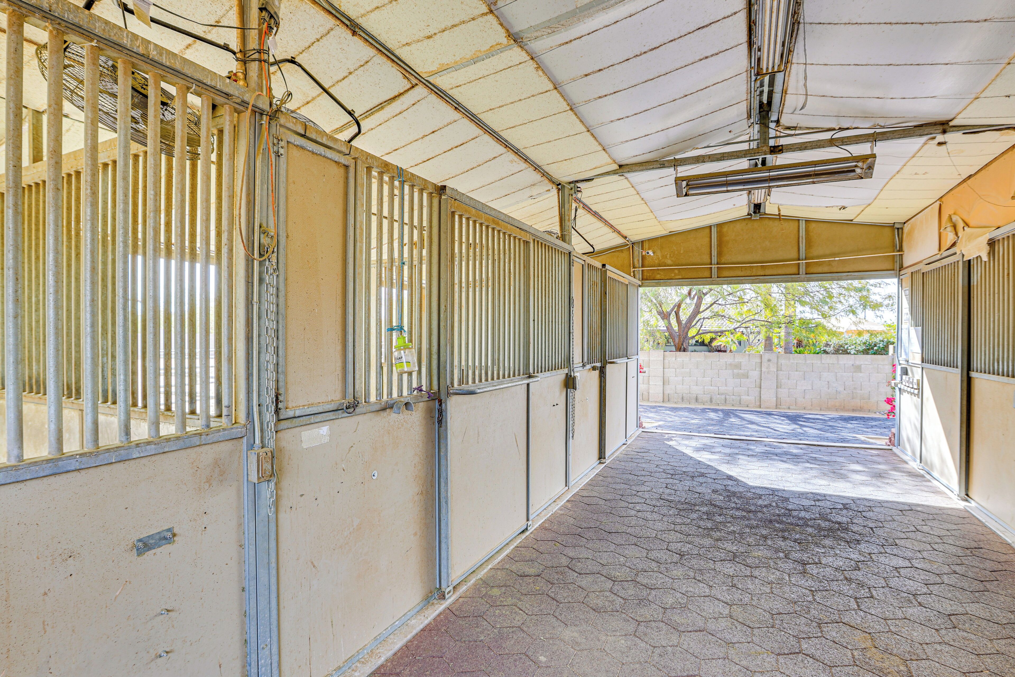 A covered stable with metal bars, a tiled floor, and a concrete wall.