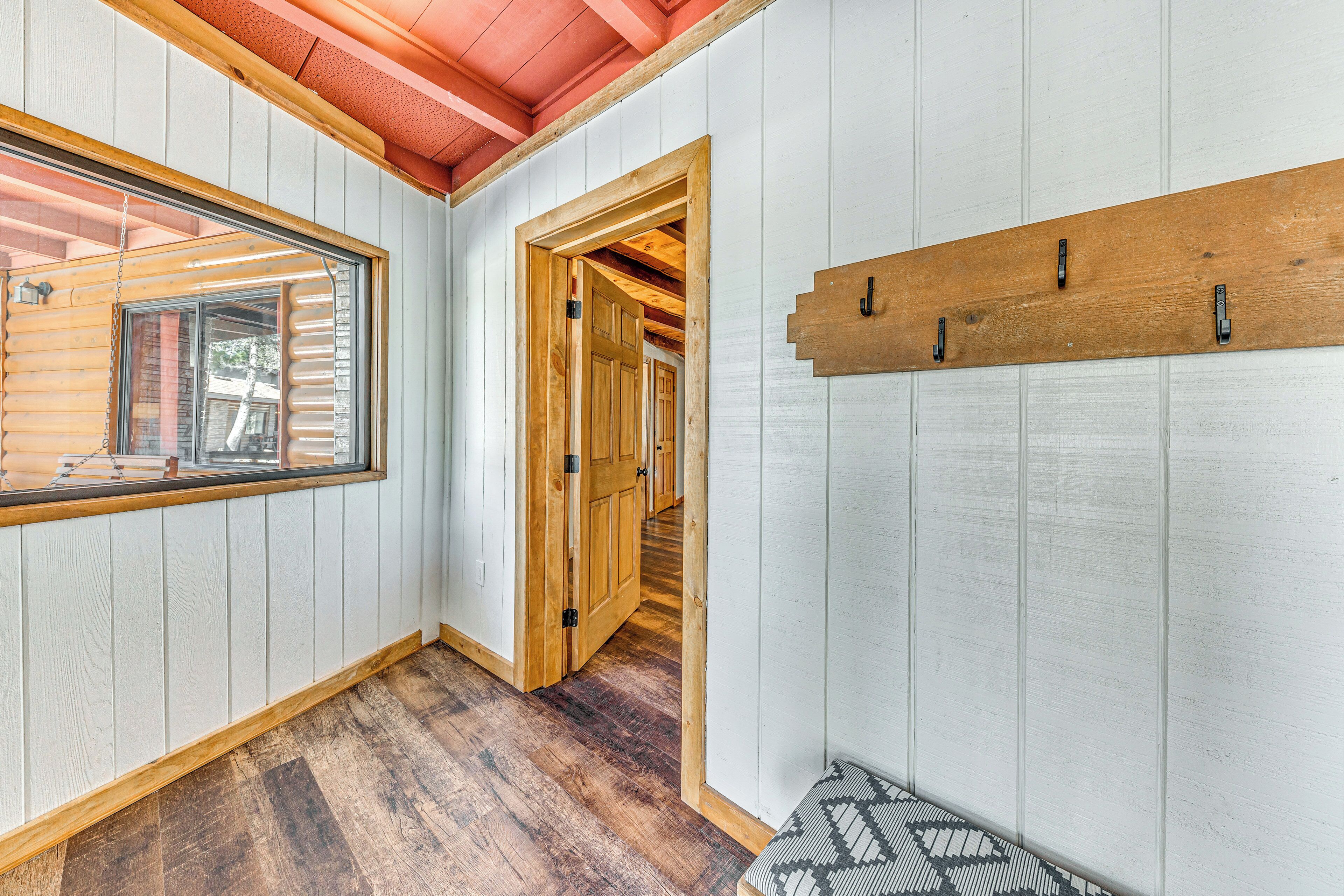 A hallway with wooden walls and a wooden ceiling, leading to a door and a bench.
