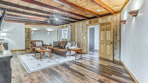 A spacious living room with a wooden ceiling and hardwood floors, featuring a leather sofa, a coffee table, and a rug.