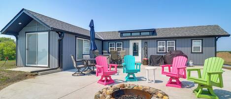 A modern house with a fire pit and colorful Adirondack chairs.