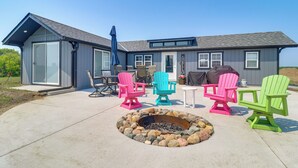 Een huis met een overdekte patio, voorzien van kleurrijke Adirondack-stoelen, een vuurkorf en een eettafel met stoelen.