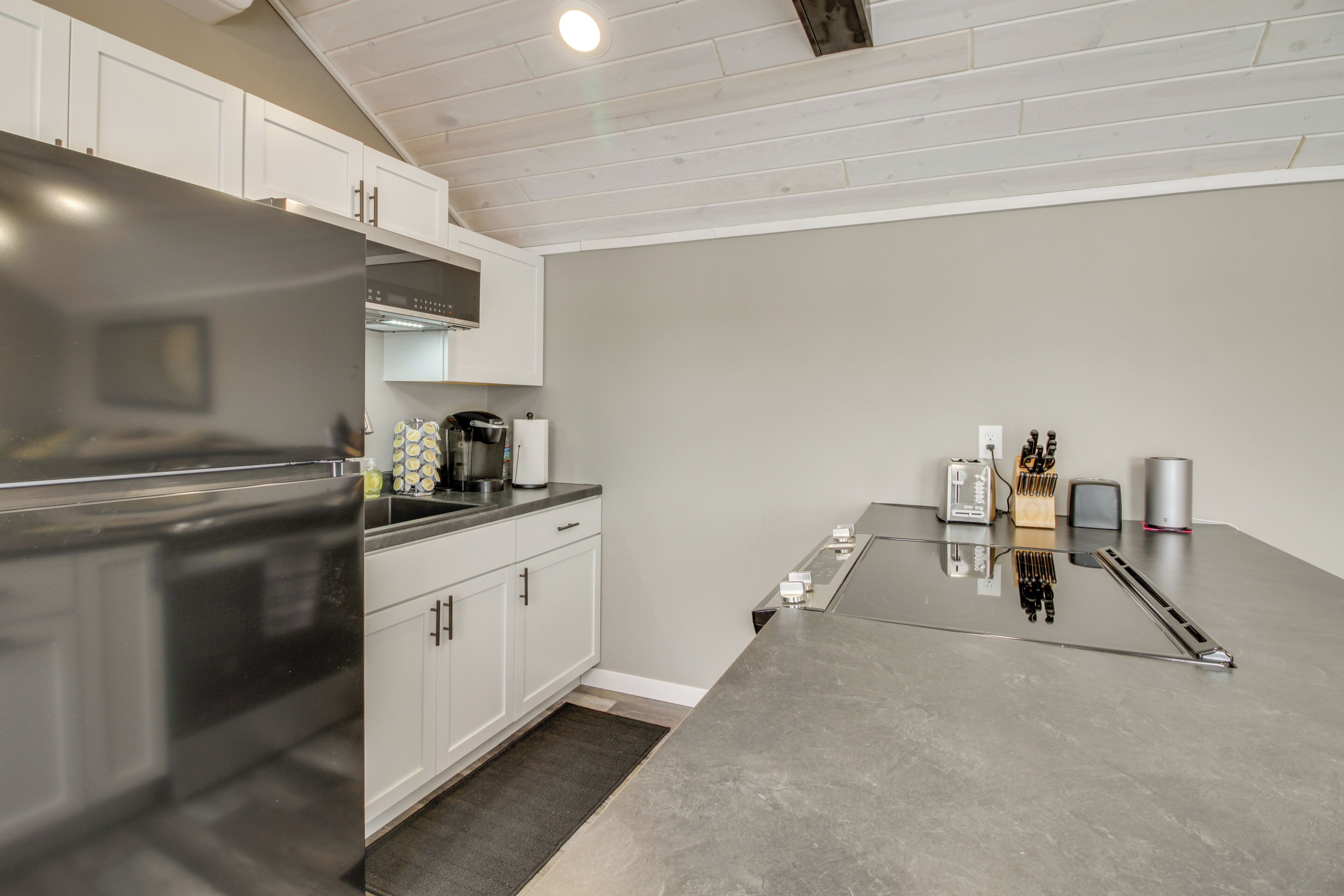A modern kitchen with white cabinets, a stainless steel refrigerator, and a grey countertop.