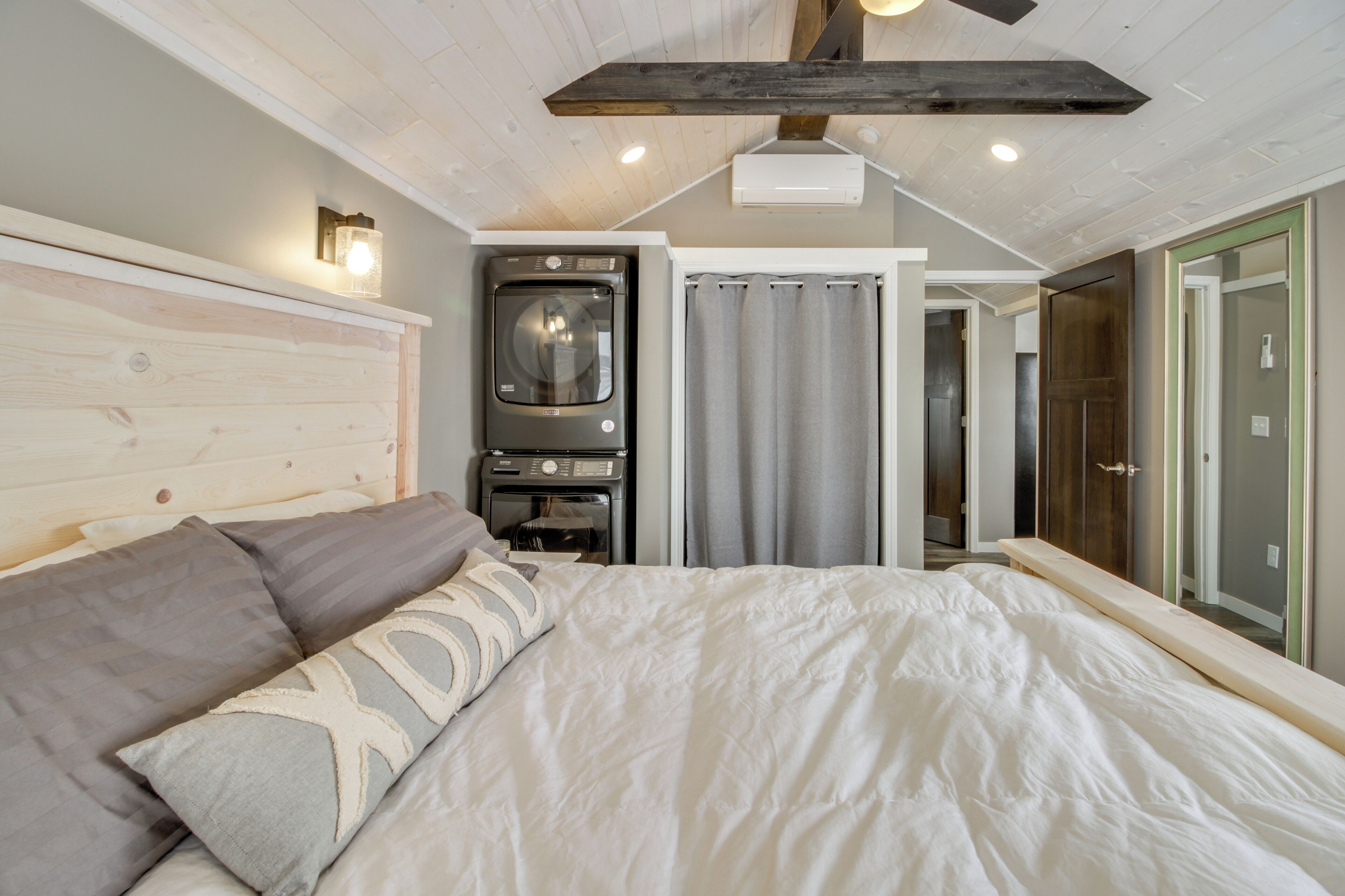 A bedroom with a bed, a washing machine, and a mirror.