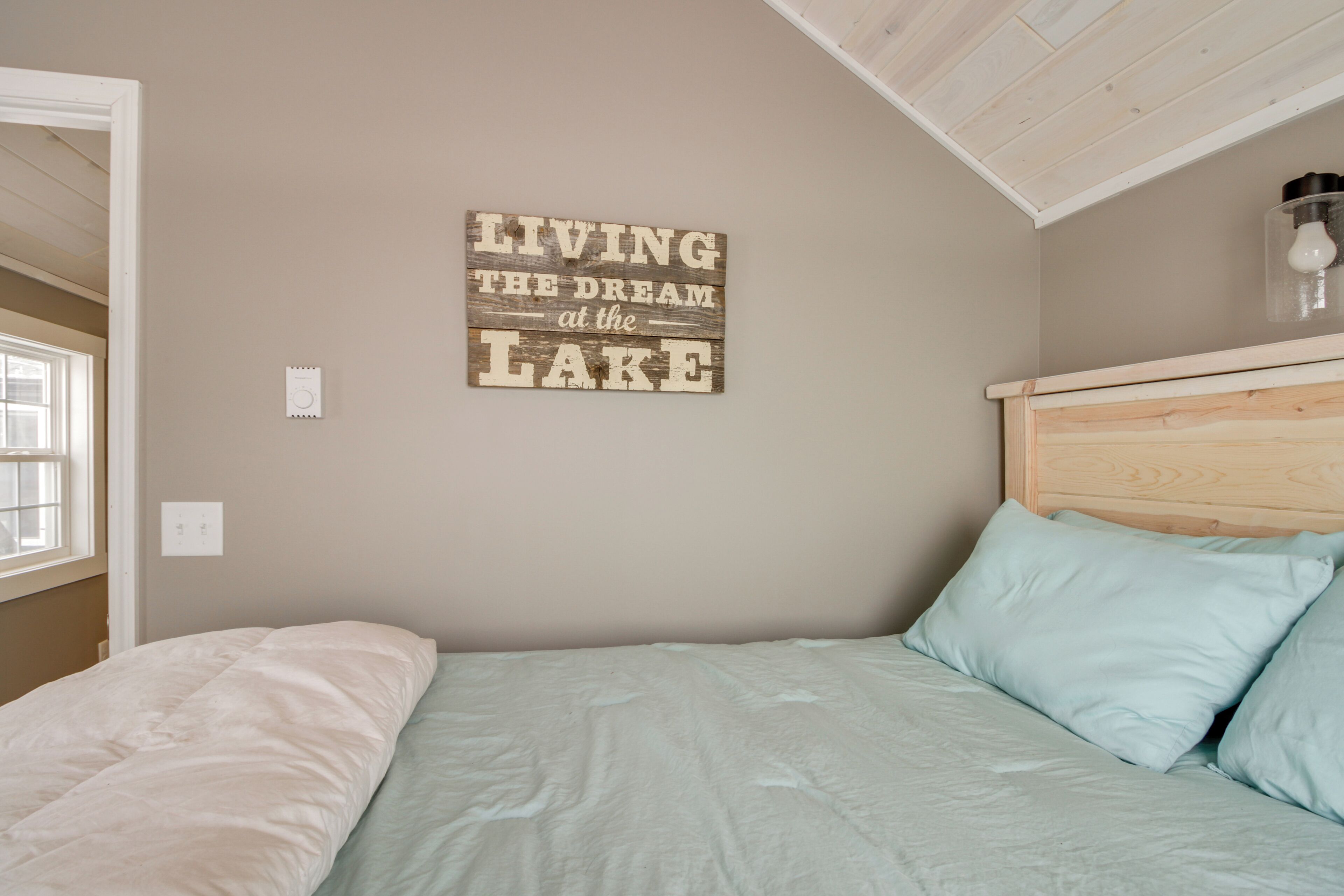 Un dormitorio con una cama, cabecera, un letrero en la pared y una ventana.