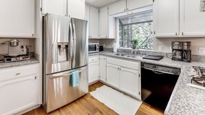 Una cocina moderna con armarios blancos, electrodomésticos de acero inoxidable y un ventanal que aporta luz natural.