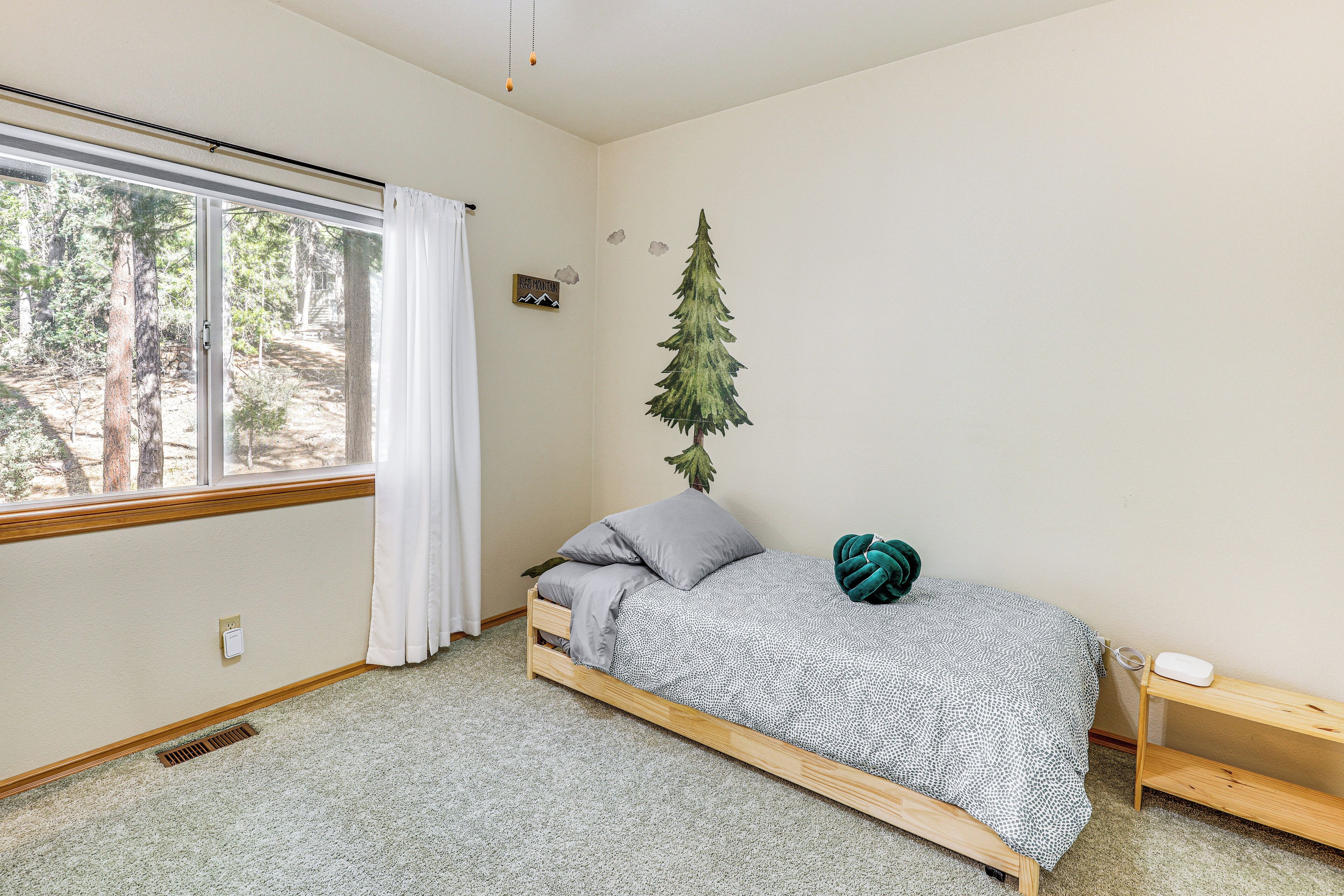 A bedroom with a bed, a window, a wall-mounted plant, and a small shelf.