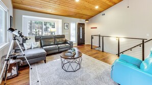 Un salón amplio con techo de madera, un sofá de cuero, un sillón azul y un trípode con una cámara.