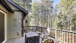 Una terraza de madera con mobiliario exterior, una mesa cubierta y vistas a un área boscosa.