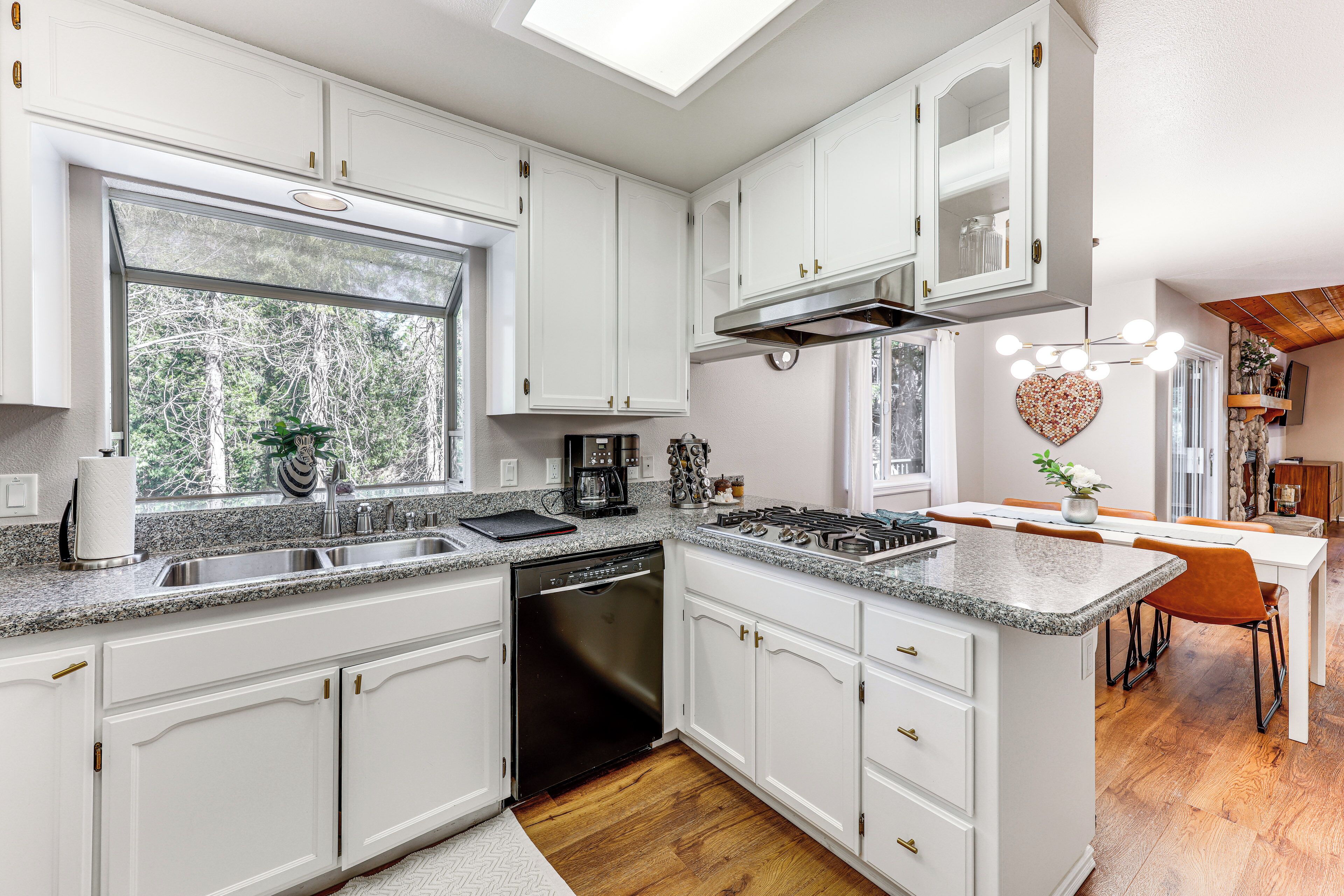 A modern kitchen with white cabinetry, a dishwasher, a stove, and a dining area with a table and chairs.