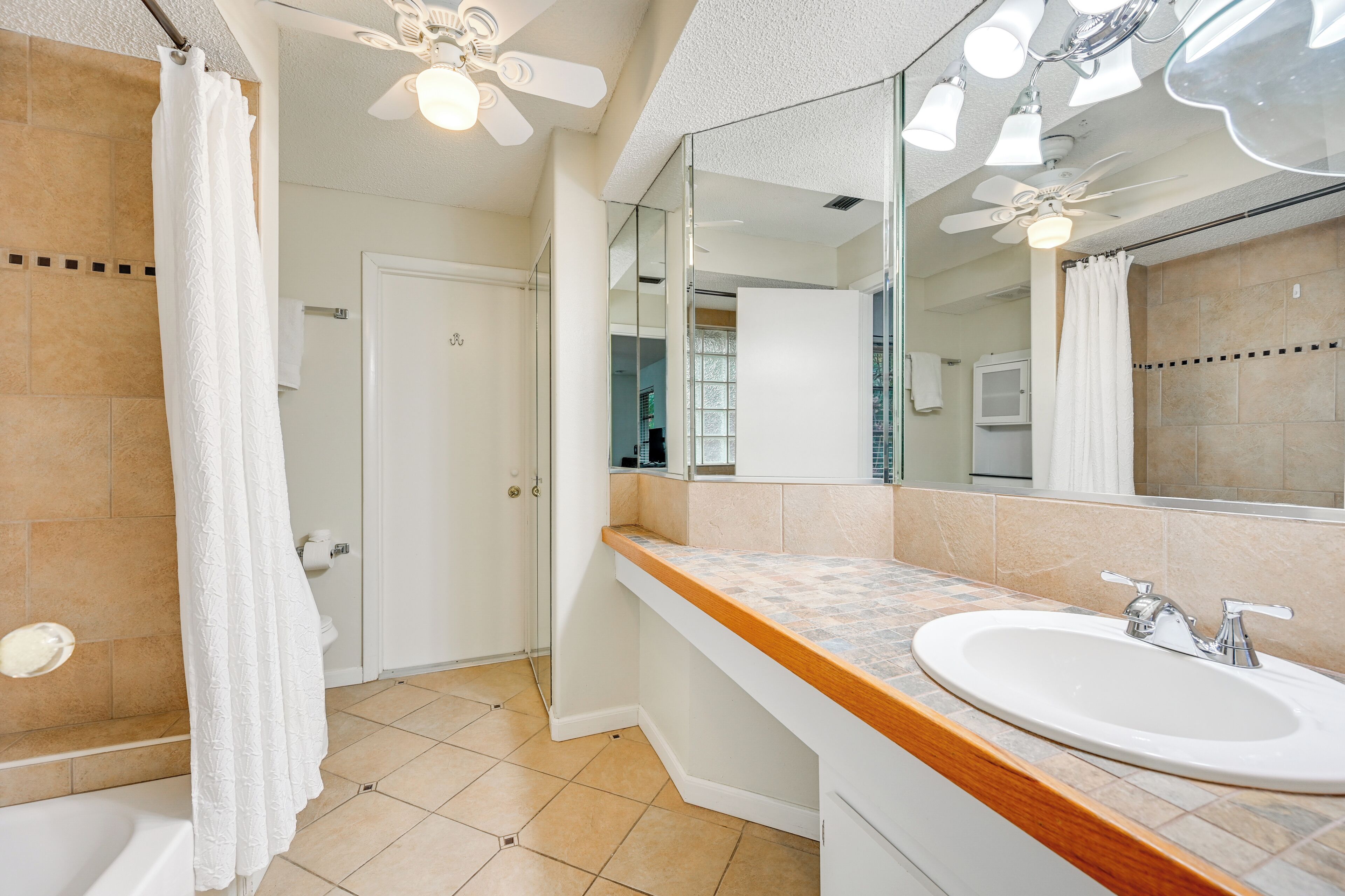 Une salle de bain avec une baignoire, un lavabo, un miroir et un ventilateur de plafond.