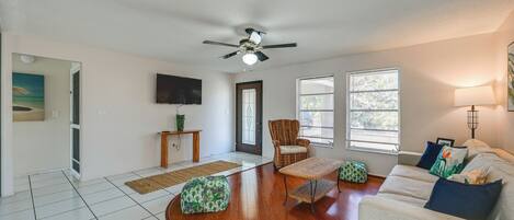 A living room with a ceiling fan, a sofa, a chair, a coffee table, and a television mounted on the wall.