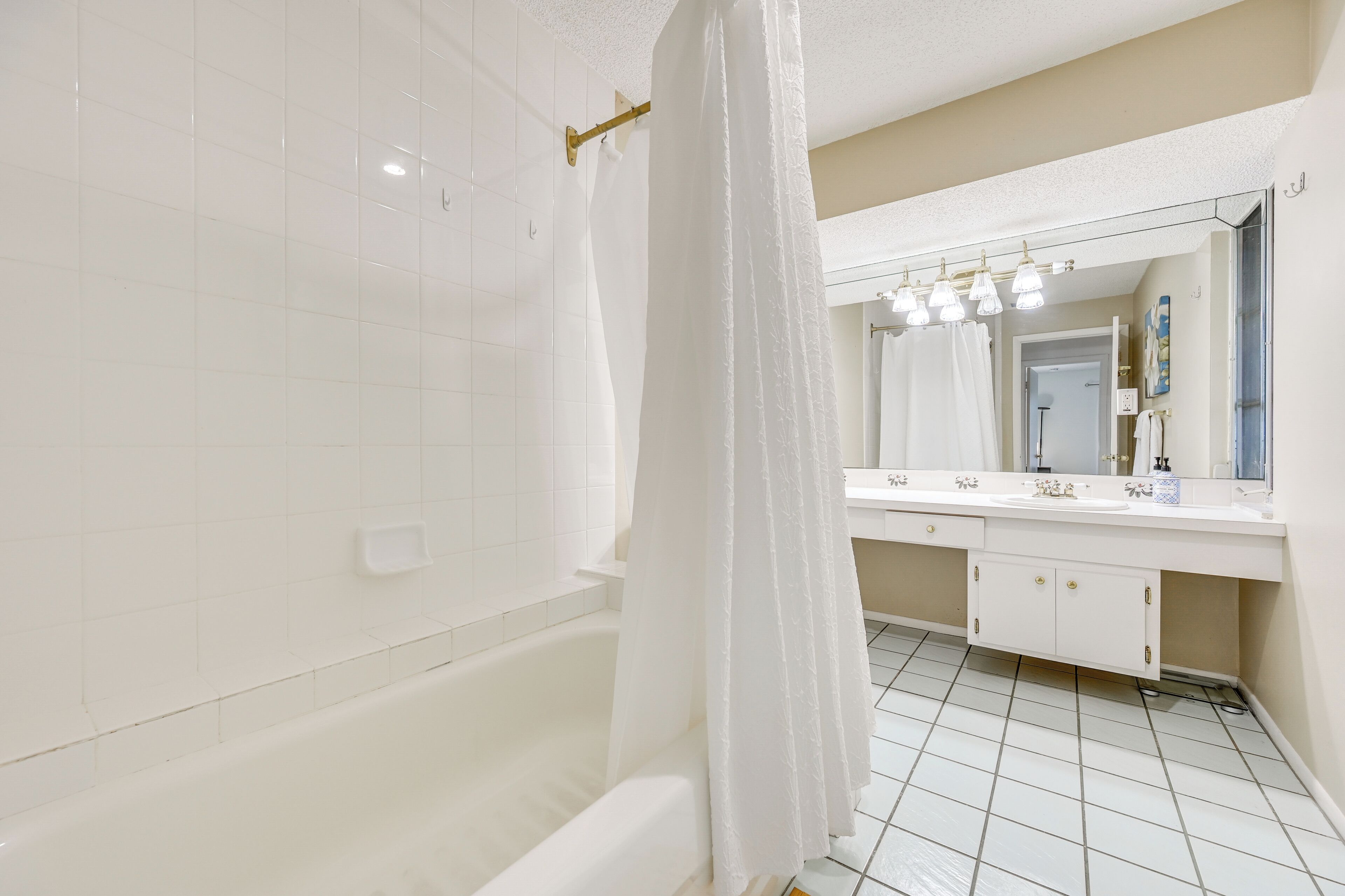 A modern bathroom with a bathtub, a large mirror, and a white tiled floor.