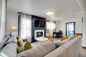 A living room with a sofa, a fireplace, a television, and a dining area. - Fire Pit & River View: Serene Stay in Seaside! (Seaside)