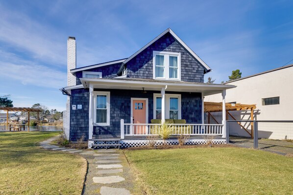 A two-story house with a dark blue exterior, a white front porch, and a chimney. - Fire Pit & River View: Serene Stay in Seaside! (Seaside)