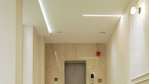 A hallway with a marble floor, a green sofa, and an elevator. - Hotel Suryodaya (Ujjain)