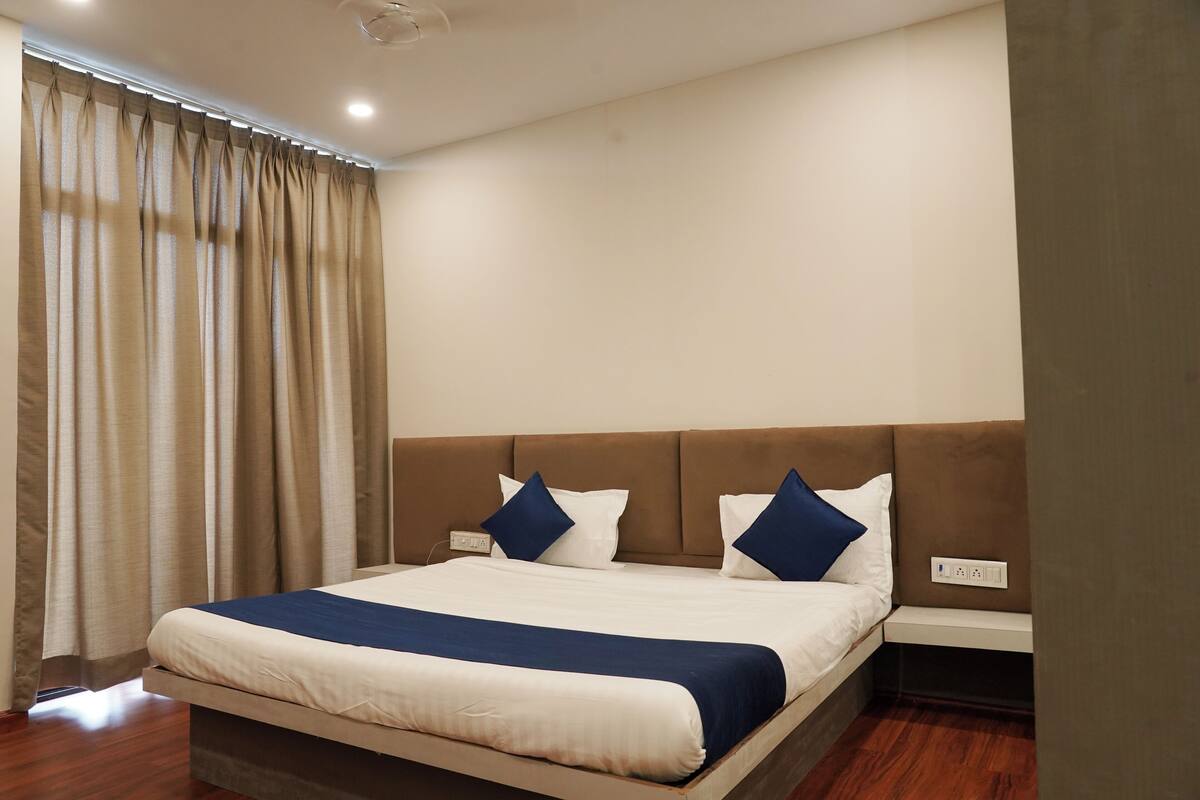 A neatly made bed with a headboard, a bedside table, and a power outlet on the wall.