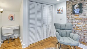 A room with a white desk, a grey armchair, a wooden floor, a brick wall, and a white closet with sliding doors. - 4 Mi to Kentucky Derby: Home w/ Private Yard (Louisville)
