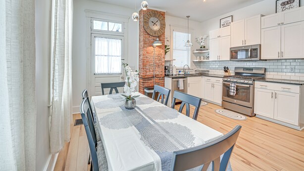 A modern kitchen with white cabinets, a brick accent wall, a large clock, and pendant lighting. - 4 Mi to Kentucky Derby: Home w/ Private Yard (Louisville)