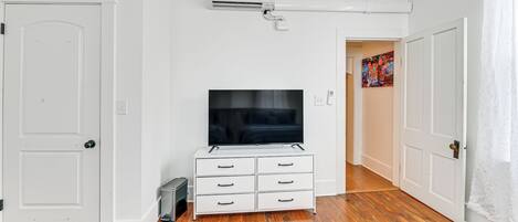 Et værelse med hvide vægge, et fladskærms-TV på en hvid kommode, en hvid dør og en hvid gardin.