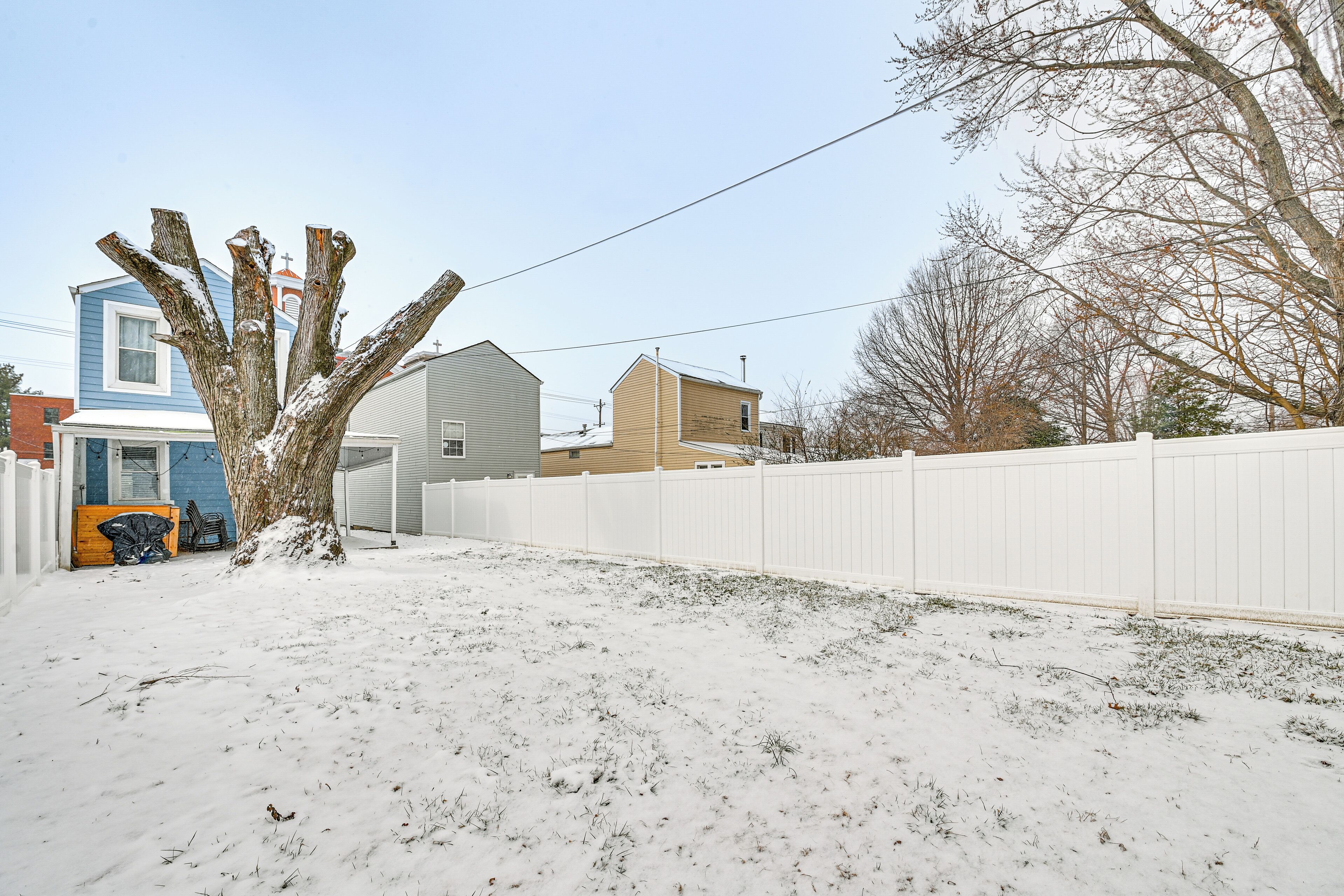 A snow-covered yard with a white fence, a tree, and houses in the background.
