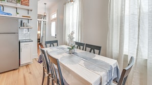A modern kitchen with white cabinets, a refrigerator, and a dining area with a table set for four. - 4 Mi to Kentucky Derby: Home w/ Private Yard (Louisville)